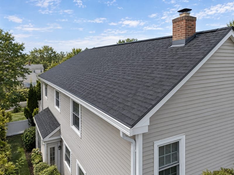 Two-story house with a newly installed charcoal architectural shingle roof, chimney flashing and gutters